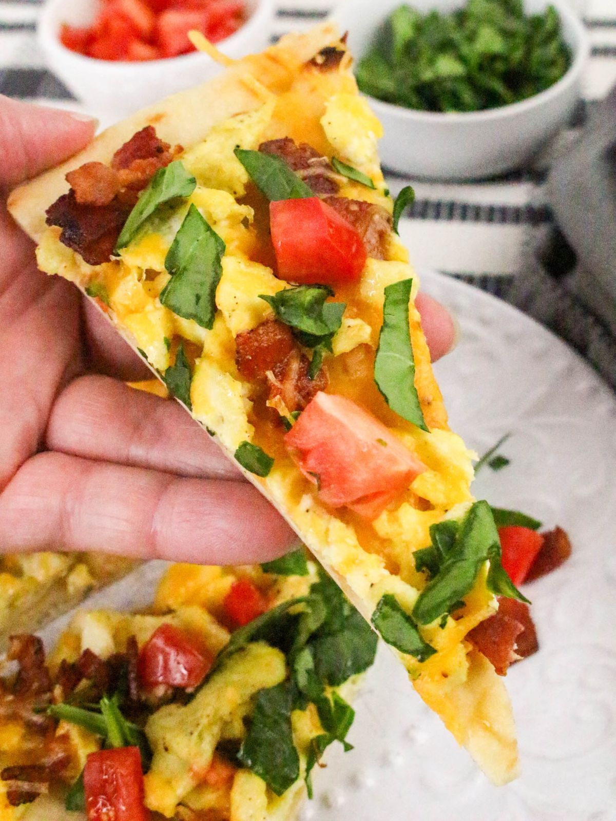 A hand holding a slice of breakfast flatbread.