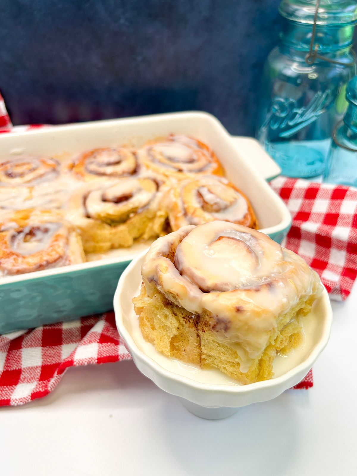 Cinnamon Rolls with Creamer in a teal baking dish with one taken out to be served.
