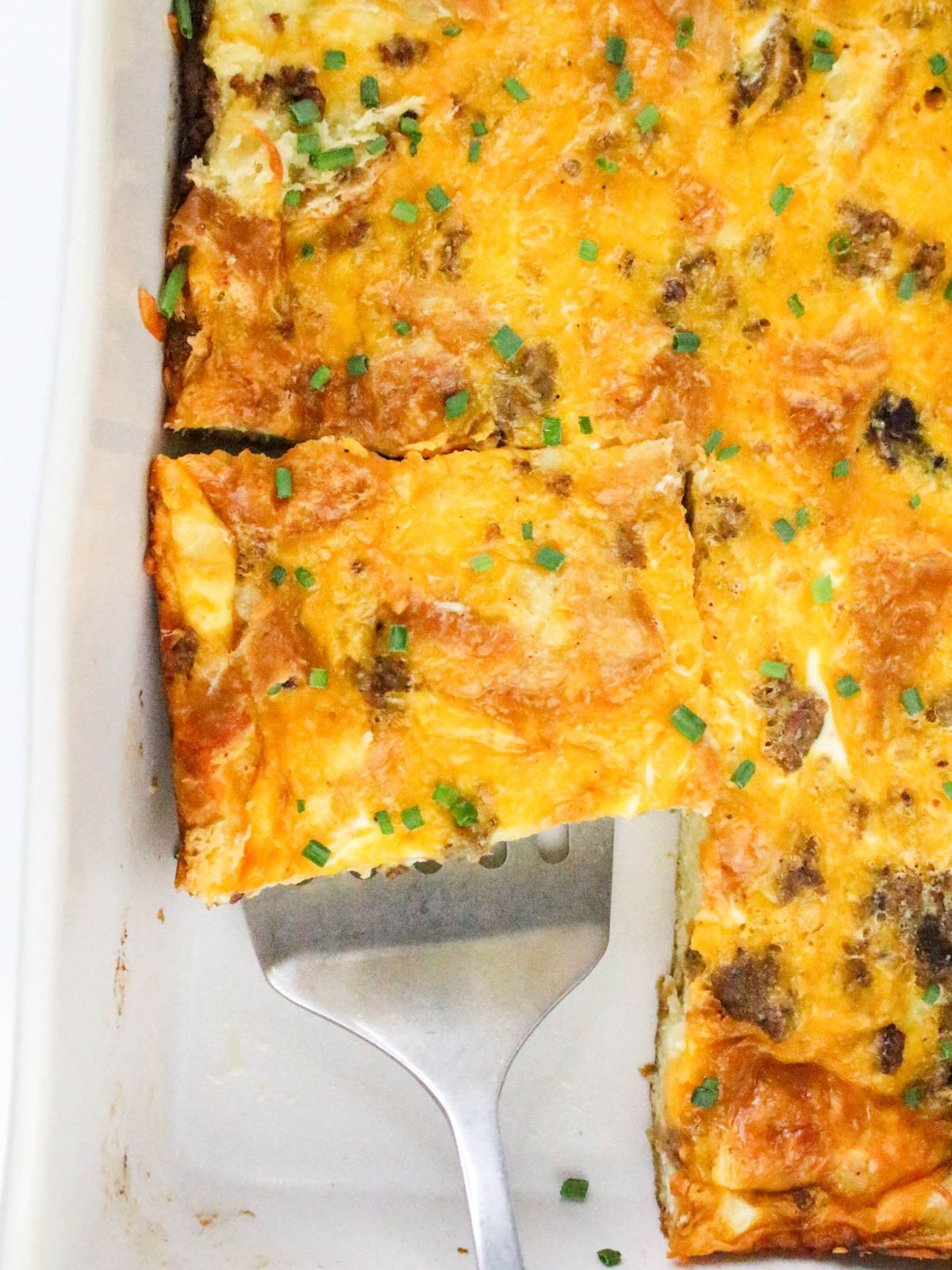 Overhead view of a spatula taking a slice of Croissant Breakfast Casserole out of the dish.
