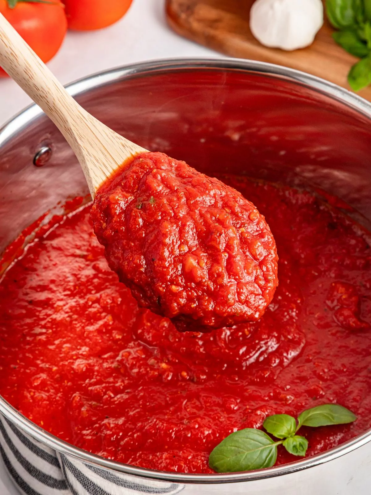 big pot of tomato sauce with wooden spoon and fresh basil leaf.