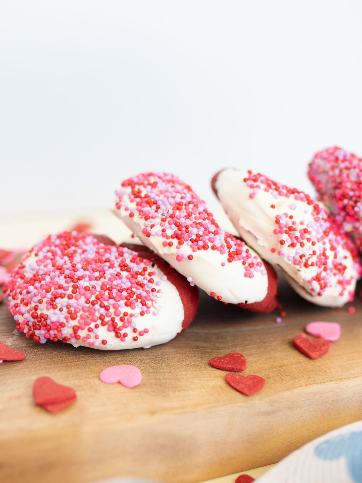 pile of Duncan Hines Red Velvet Cookies on a wood board with heart sprinkles around them.