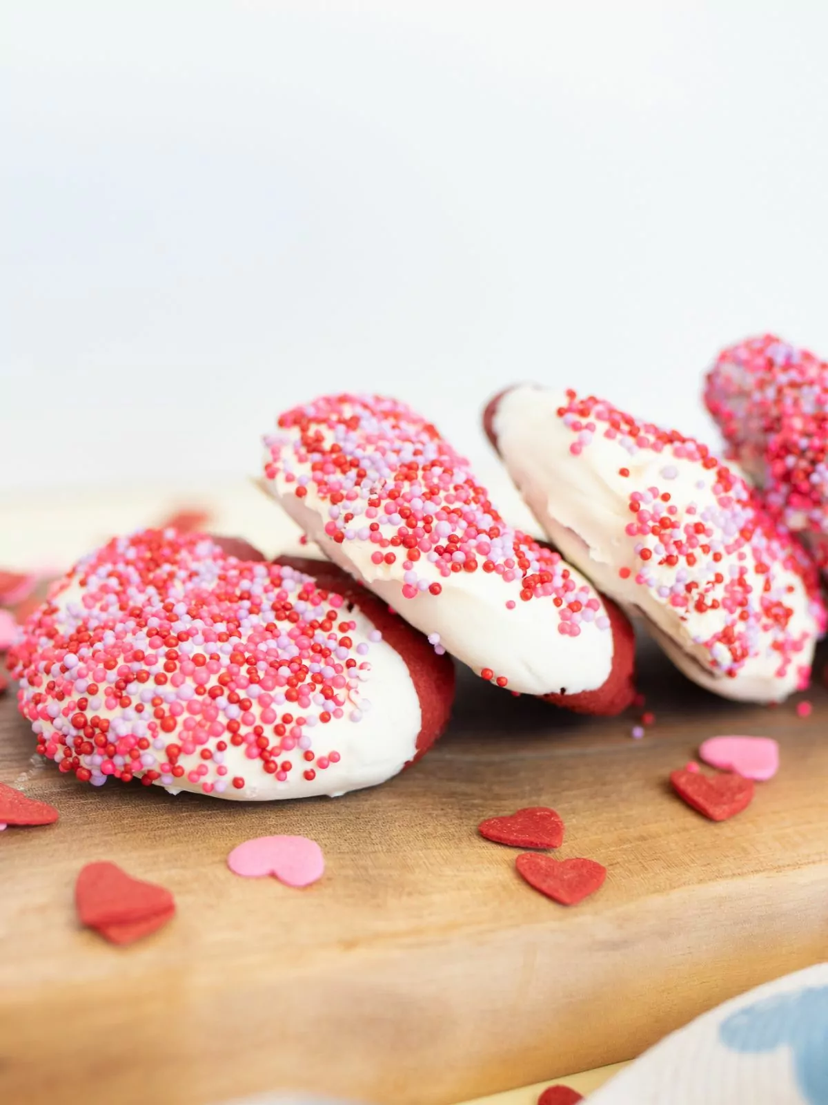 pile of Duncan Hines Red Velvet Cookies on a wood board with heart sprinkles around them.