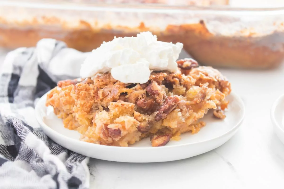 pumpkin dump cake with pecans and whipped cream on plate with black checkered napkin.