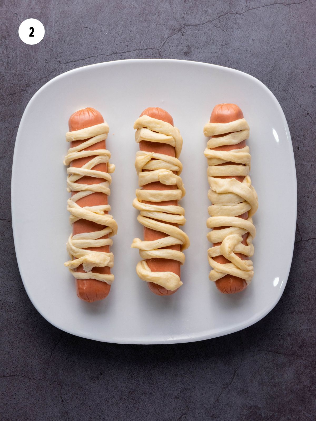 Plate of hot dogs wrapped in strips of dough.