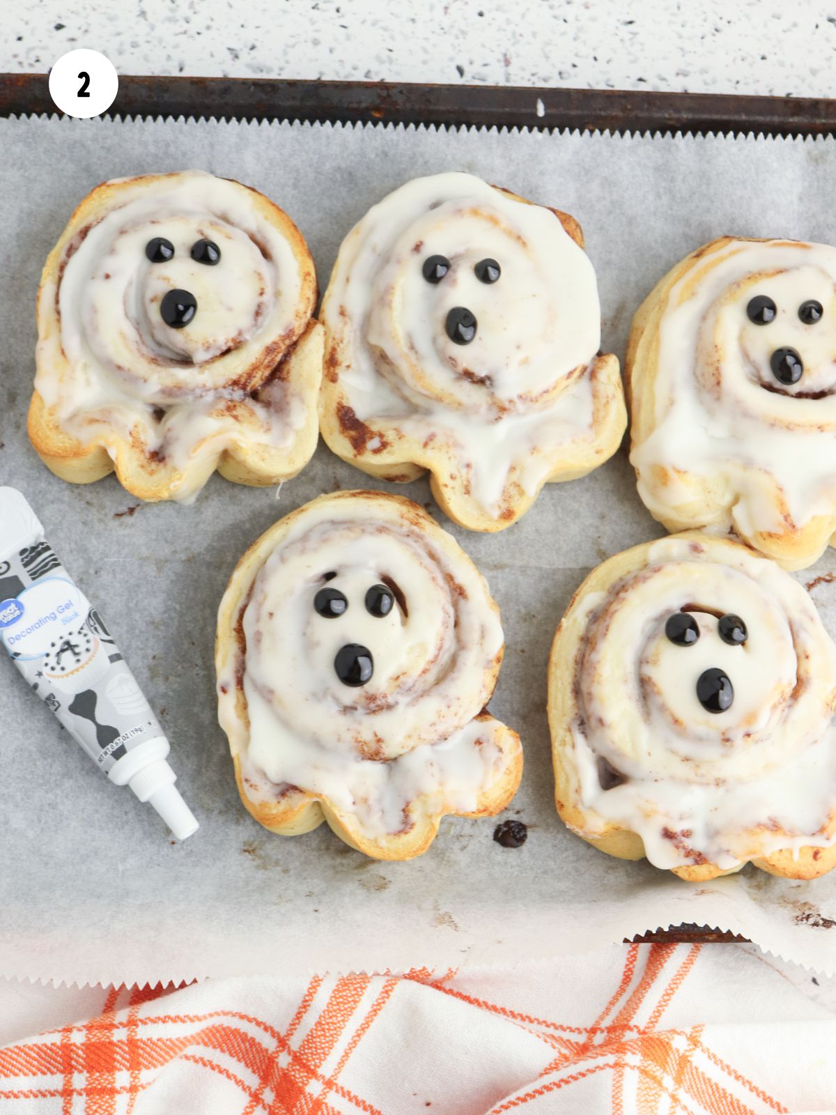 Baked cinnamon rolls with white icing spread on top and black icing dots for the eyes and mouth.