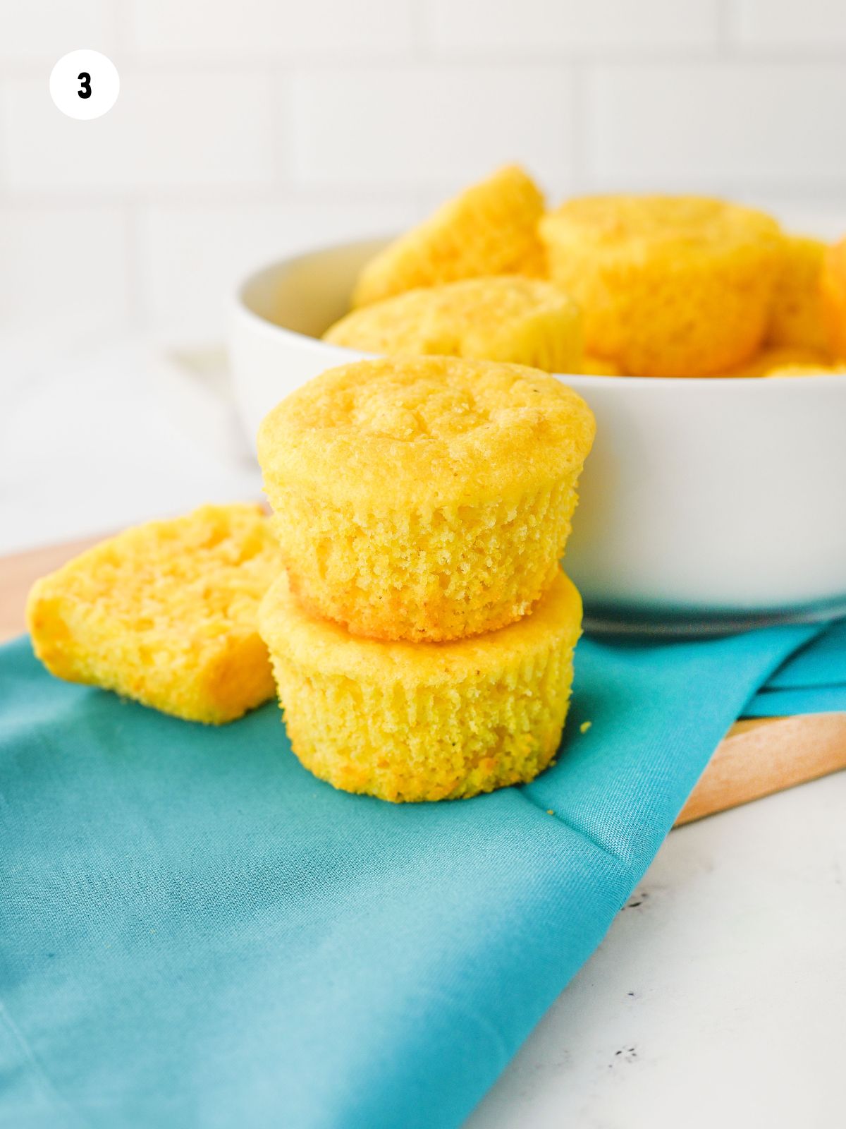 Baked cornbread muffins stacked in front of the dish with the rest of the muffins.