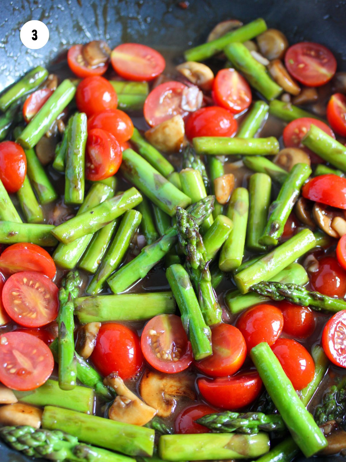 Cut asparagus, cherry tomatoes, and mushrooms cooking in a pan.