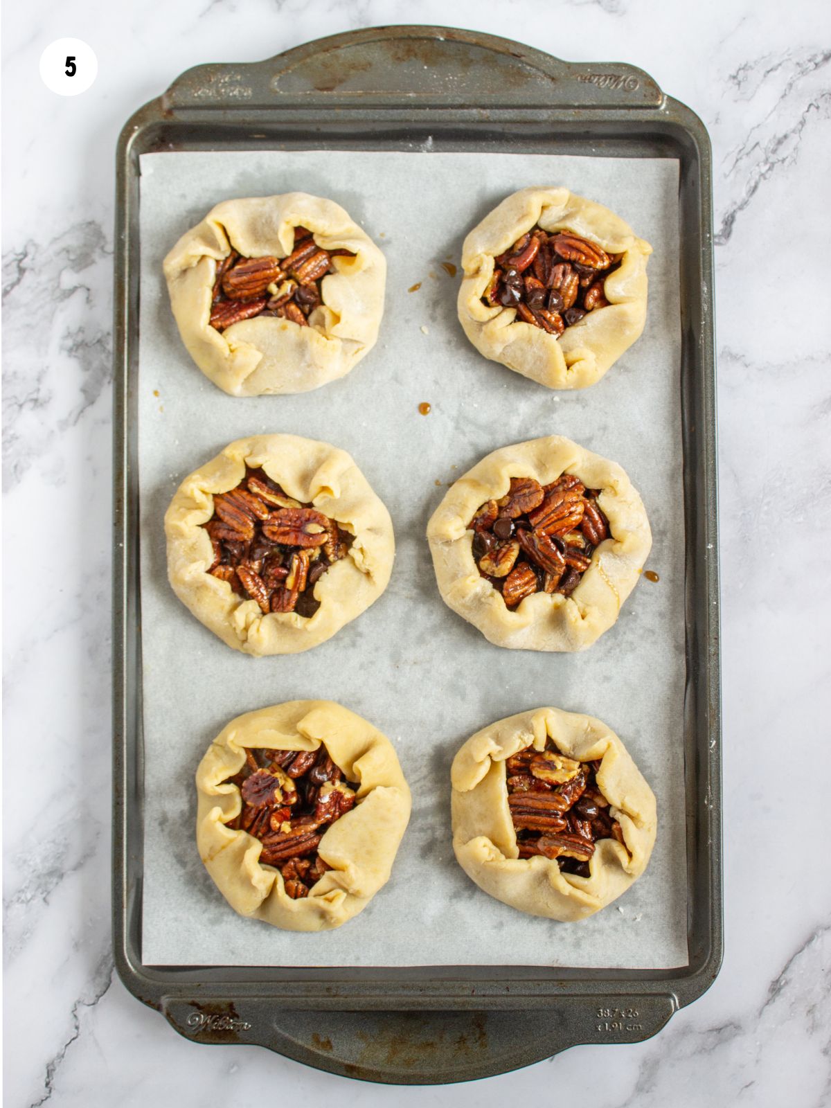 Mini rustic pecan pies on a baking tray.