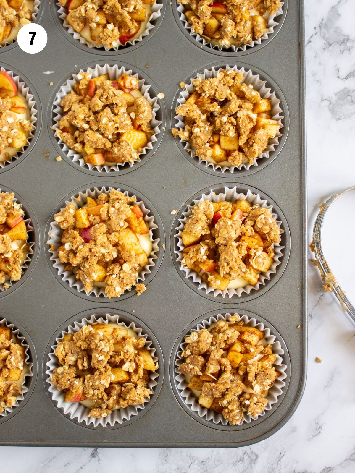 Crumb topping added on top of the apple layer in the muffin tin.