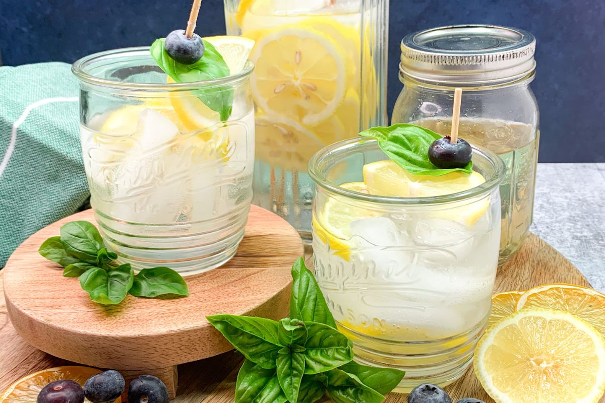2 glasses of sparkling water flavored with basil and lemon plus a pitcher of the beverage in the background.
