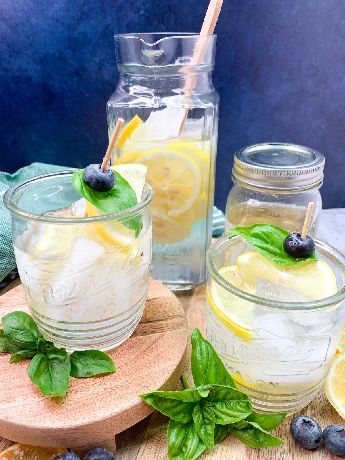 2 glasses and a pitcher of homemade sparkling water flavored with basil simple syrup and lemon slices.