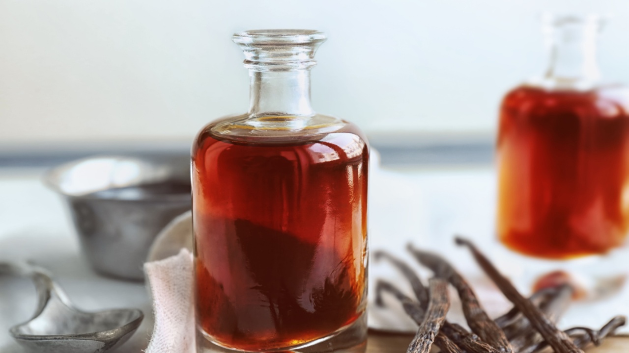 Bottle with aromatic extract and dry vanilla beans on table