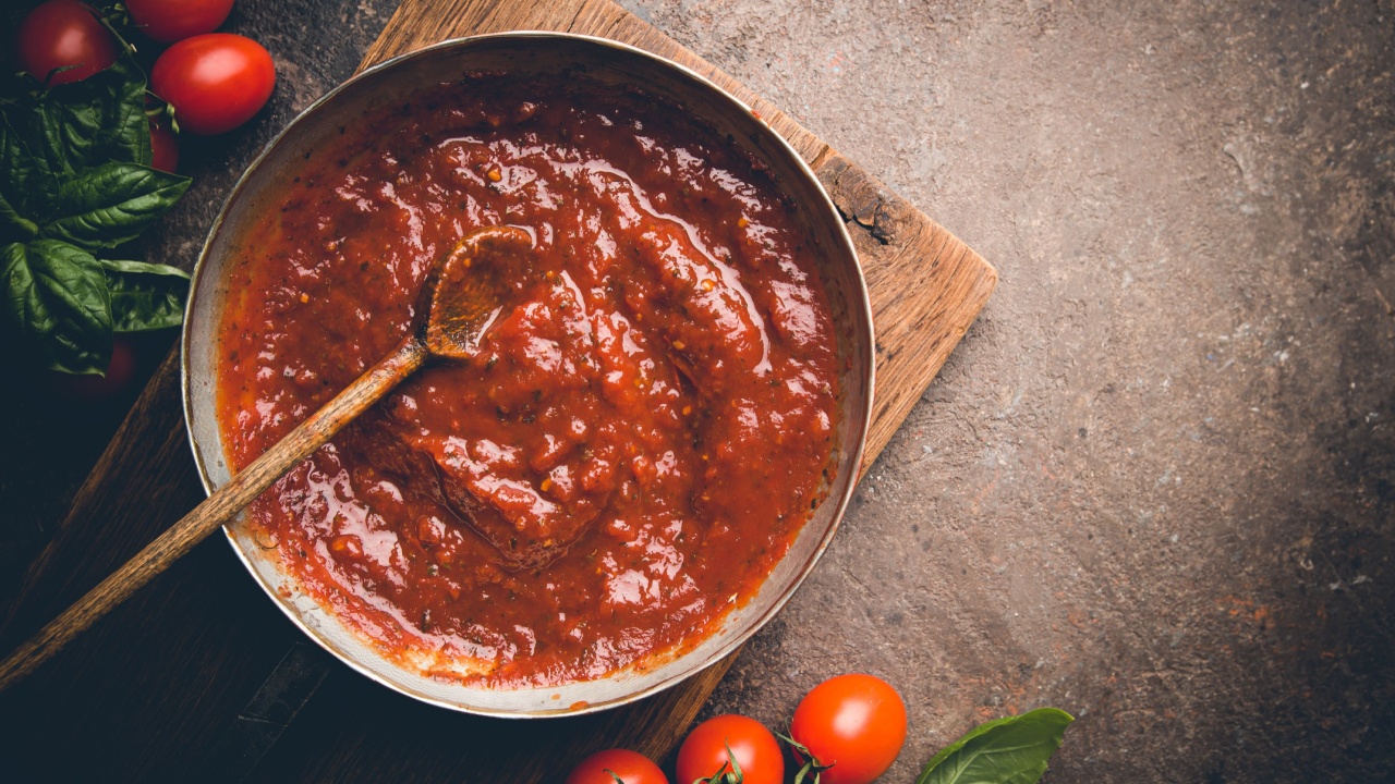 Classic homemade Italian tomato sauce with basil for pasta and pizza in the pan on a wooden chopping board on brown background, top view.