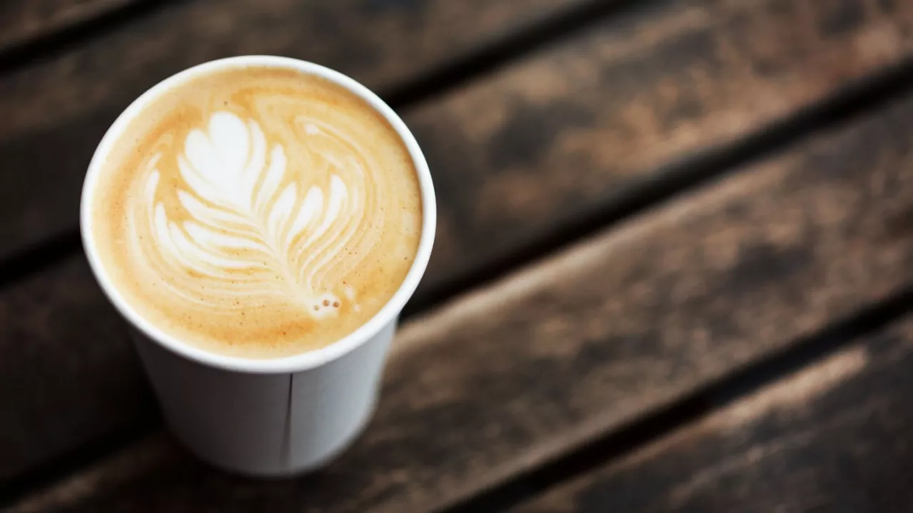 Cup of coffee to go on the wooden table with latte art. Street coffee, top view.