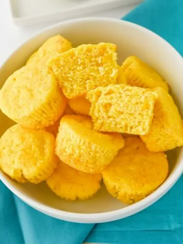 Jiffy Cornbread Muffins with Creamed Corn in a white bowl. One muffin is cut in half to show the inside.