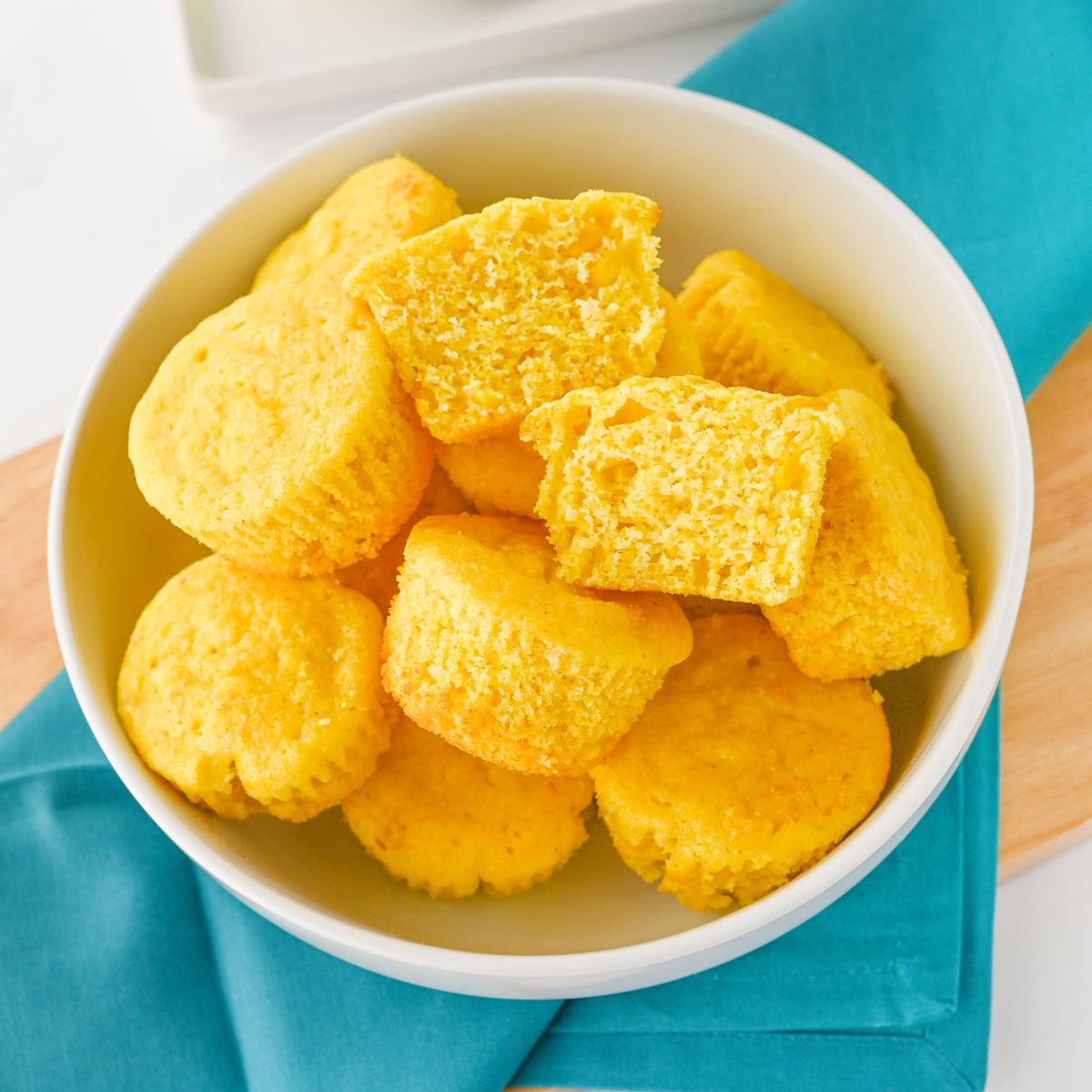 Jiffy Cornbread Muffins with Creamed Corn in a white bowl. One muffin is cut in half to show the inside.