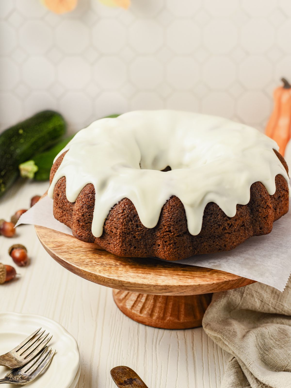 Zucchini Pumpkin Bread bundt cake topped with cream cheese frosting on a wood cake stand.