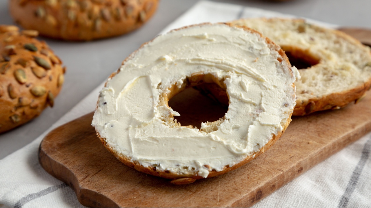 Homemade Whole Grain Bagel with Cream Cheese on a rustic wooden board, side view. Close-up.