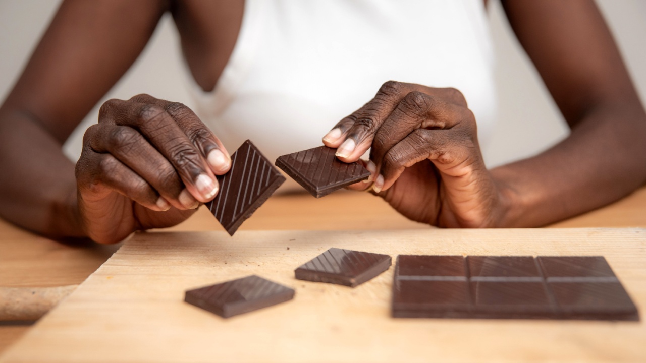 Woman Breaking a Bar of Dark Chocolate into Pieces on a Wooden Table