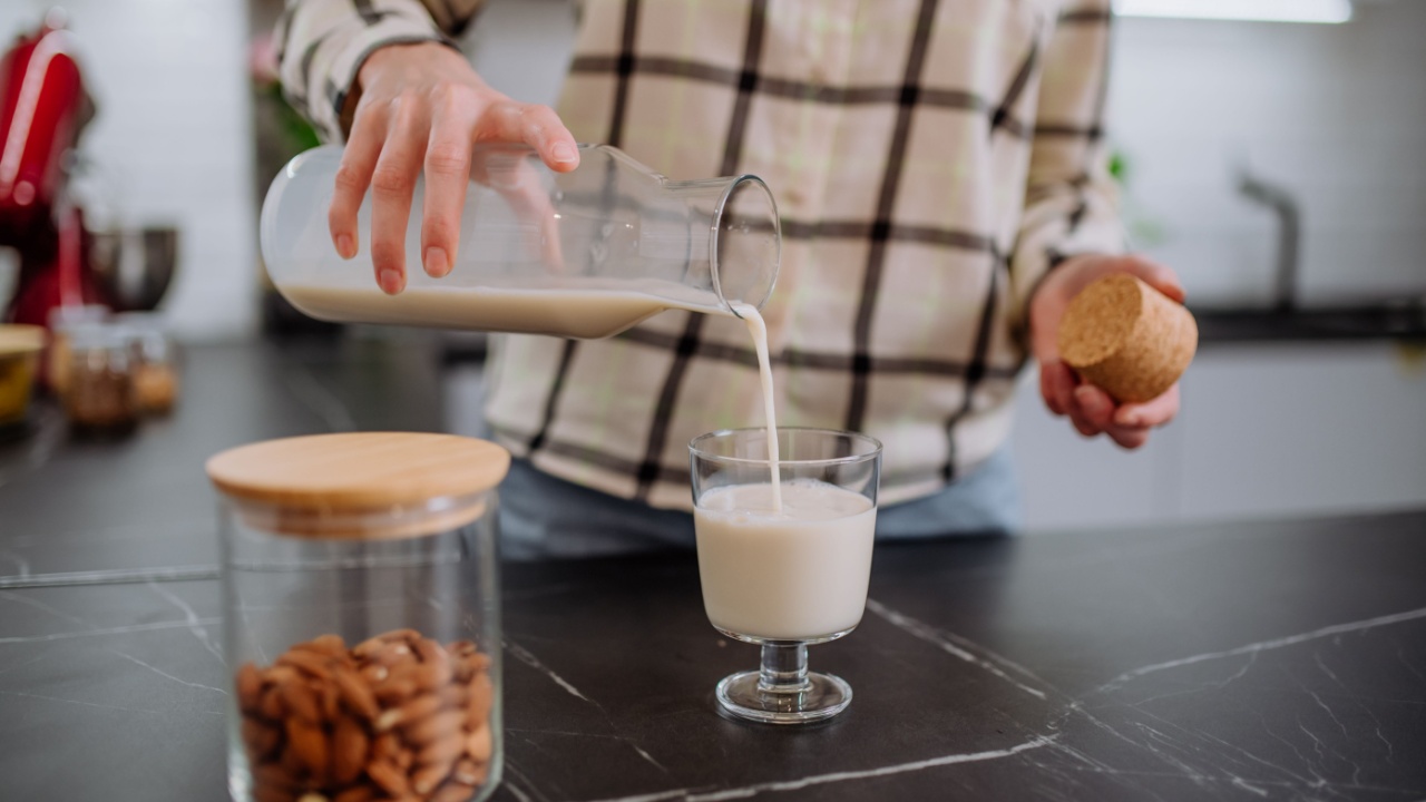 Woman pouring almond milk into a glass in kitchen. Healthy vegan product concept.