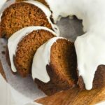 Zucchini Pumpkin bundt cake sliced on wooden plate with cream cheese frosting.