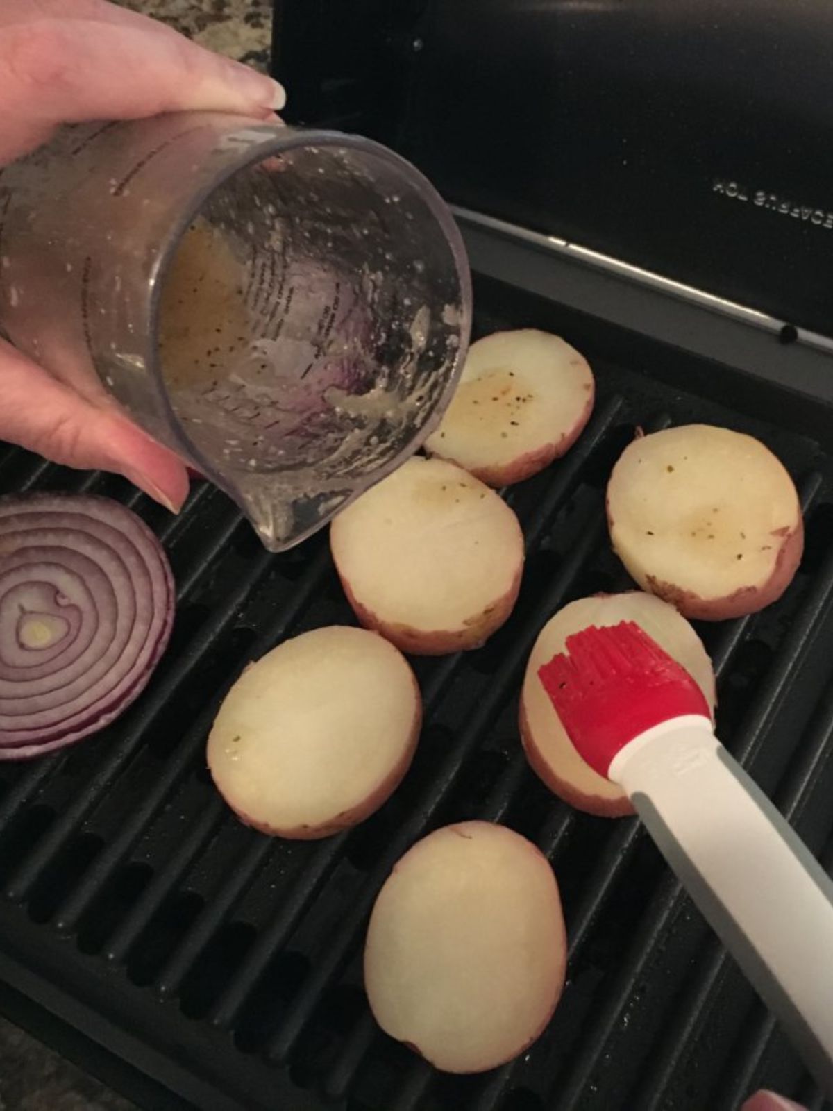 brushing Italian salad dressing on potatoes on grill.