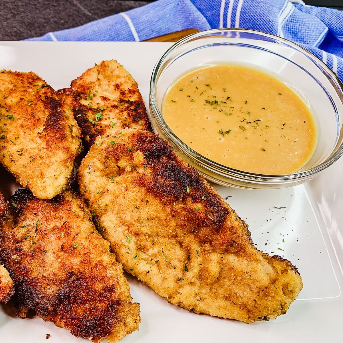 chicken cutlets on white platter with small bowl of dipping sauce.