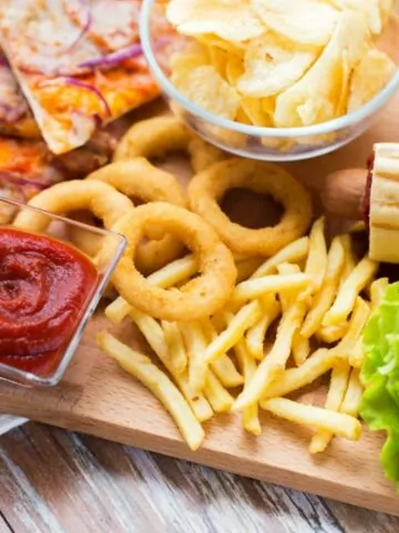 fast food and unhealthy eating concept - close up of hamburger or cheeseburger, deep-fried squid rings, french fries, pizza and ketchup on wooden table top view