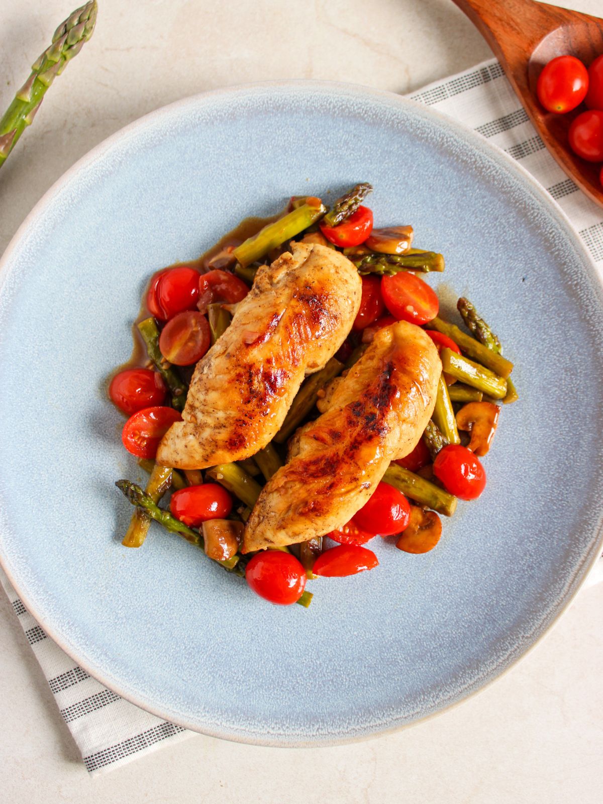 Light blue plate with 2 chicken tenderloins served on a bed of sautéed vegetables.