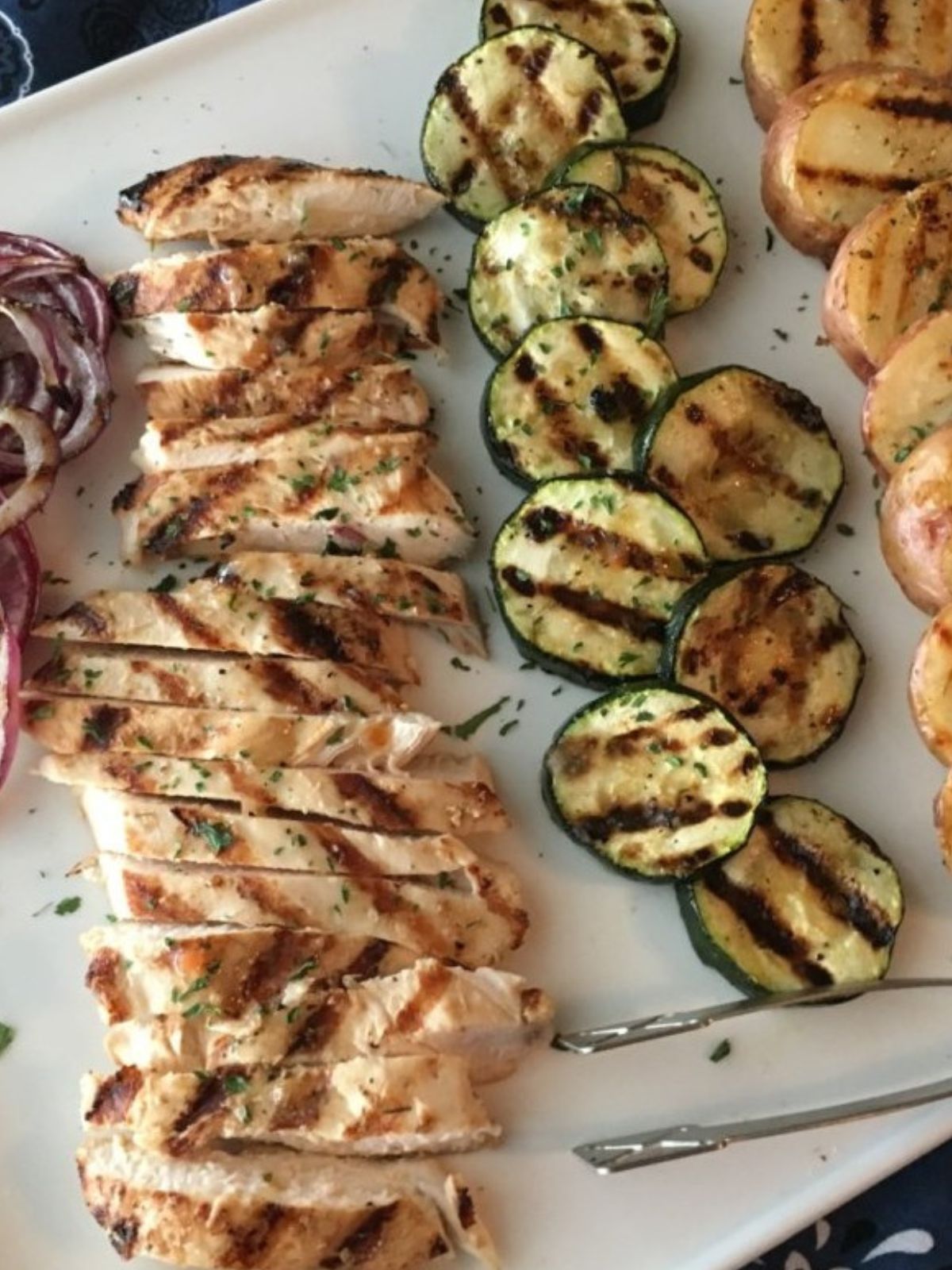 close up of grilled chicken with Italian salad dressing and veggies on white tray.