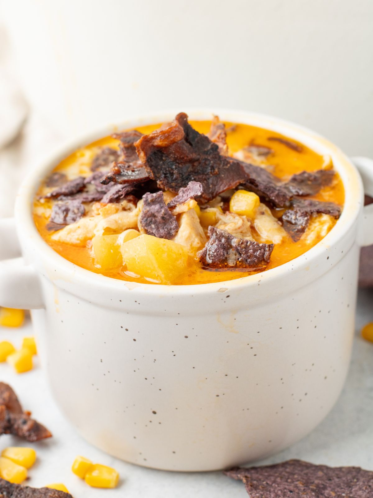 Bowl of chicken corn chowder with tortilla chips crushed on top.