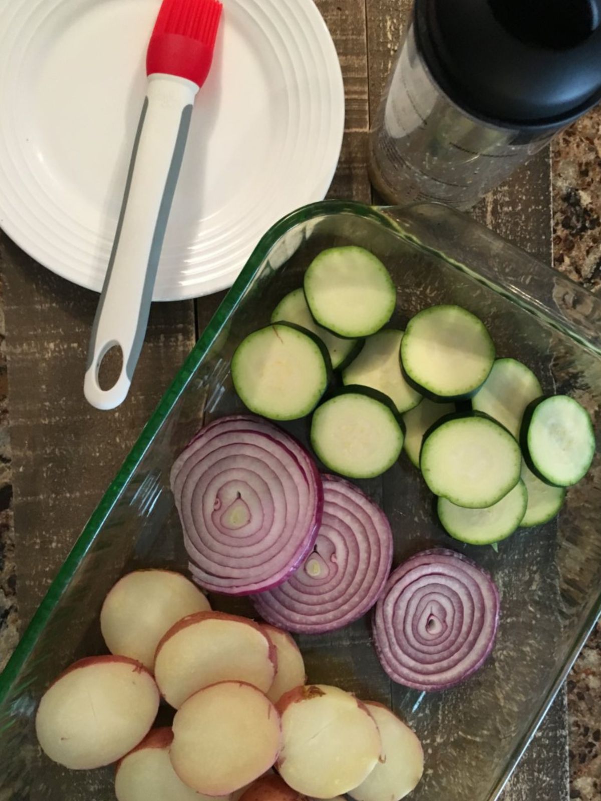 red potatoes slices, red onions slices and zucchini sliced in glass baking dish.