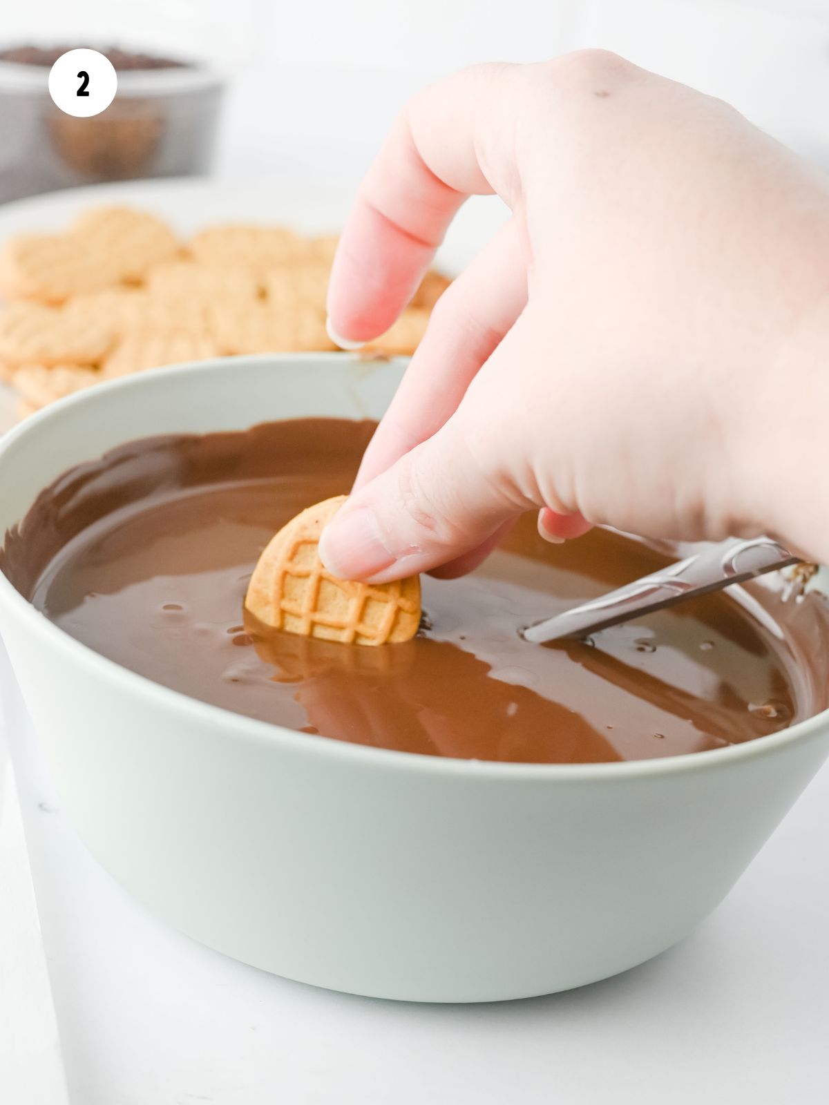 Peanut butter cookie being dipped in a bowl of melted chocolate.