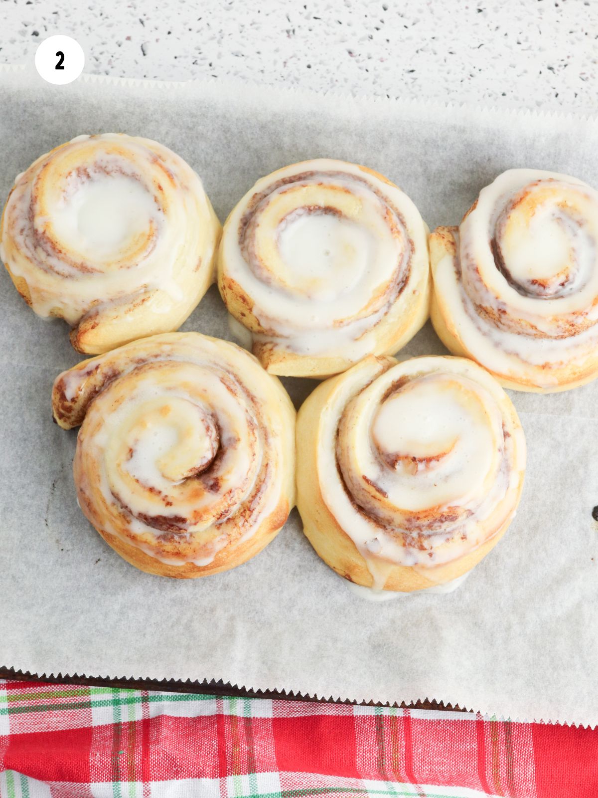 Baked cinnamon rolls with icing on baking sheet.