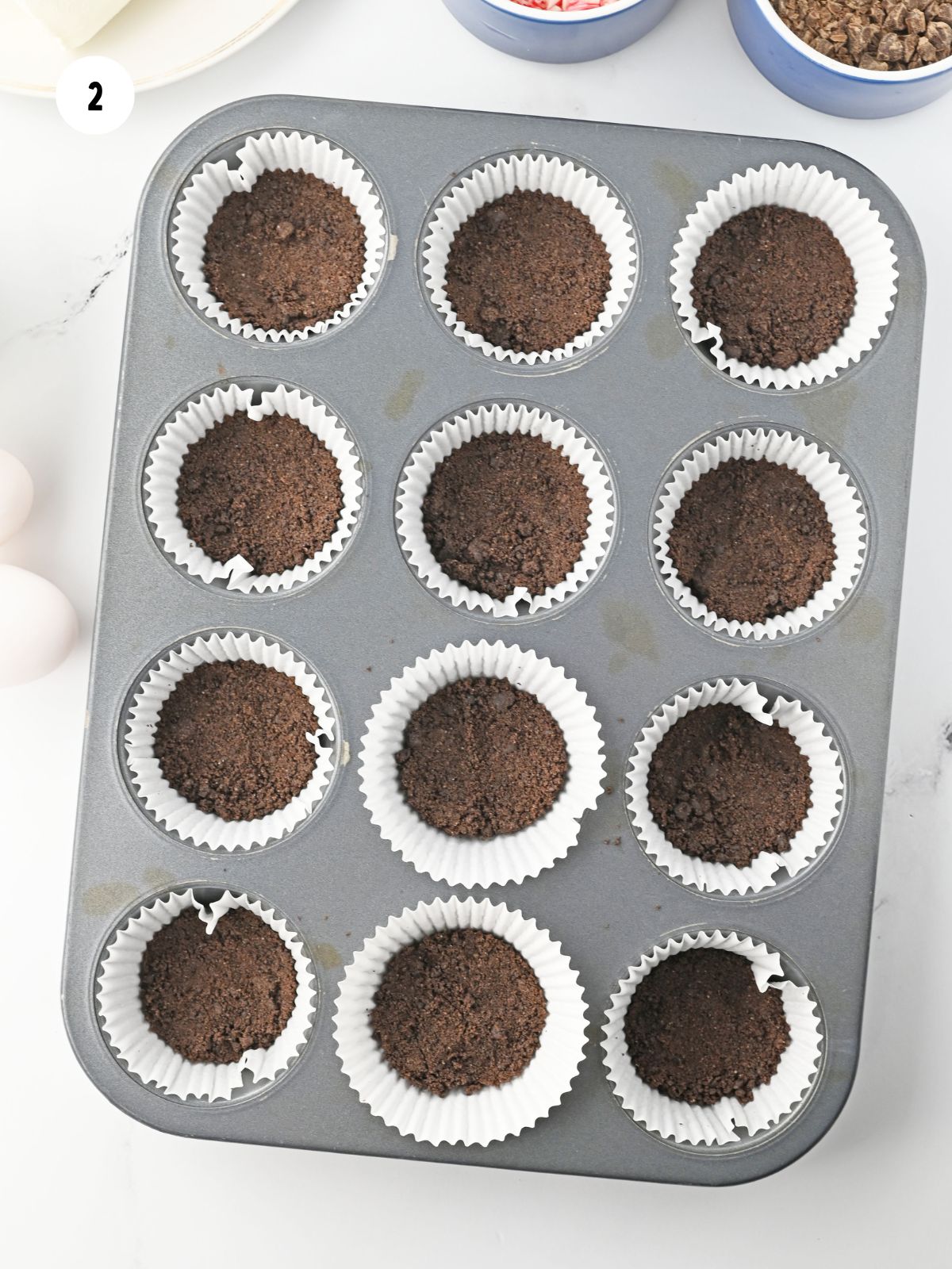 Oreo crusts pressed into liners in a muffin tin.