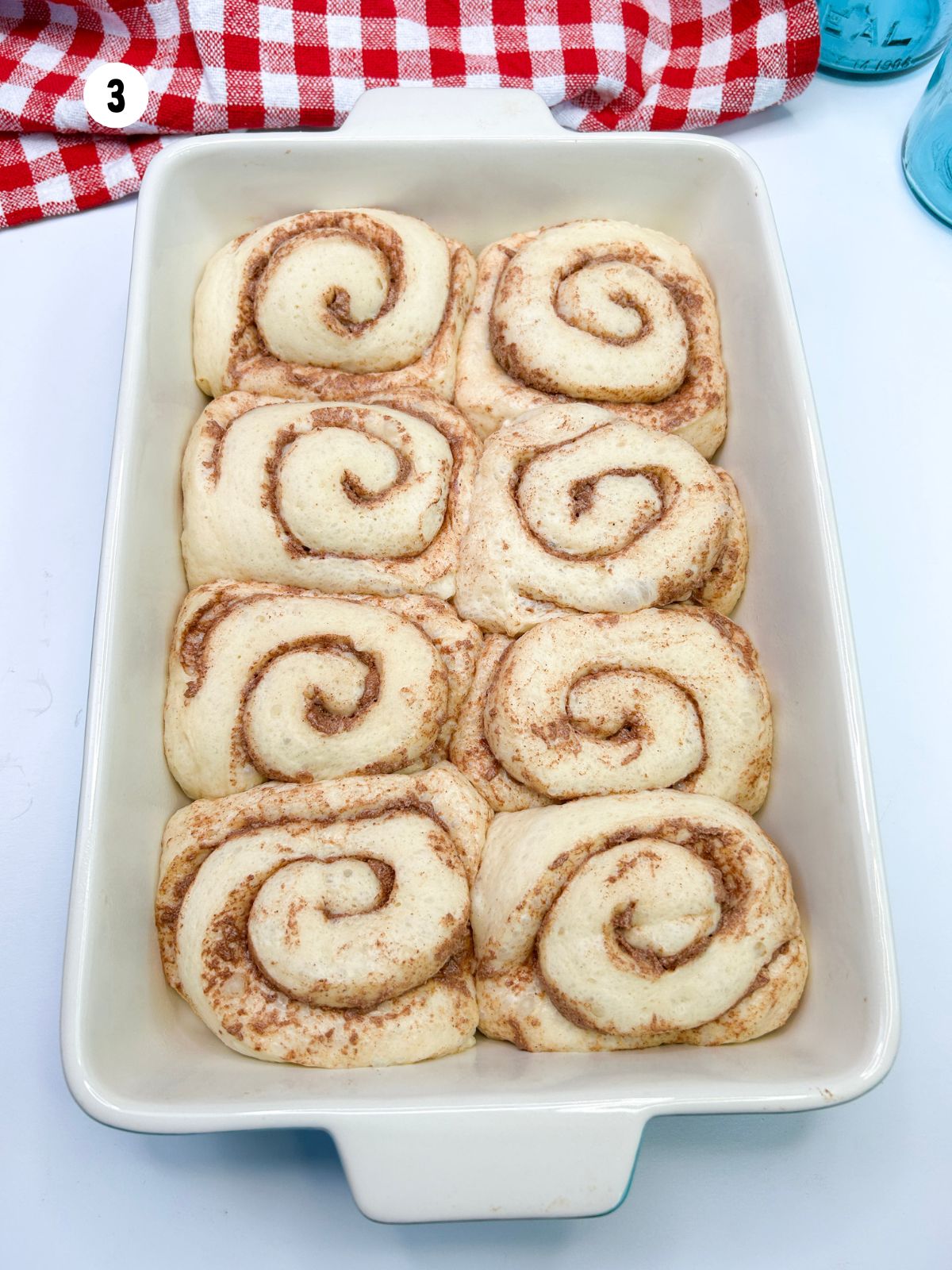 Cinnamon rolls that have risen and now touch each other in the baking dish.