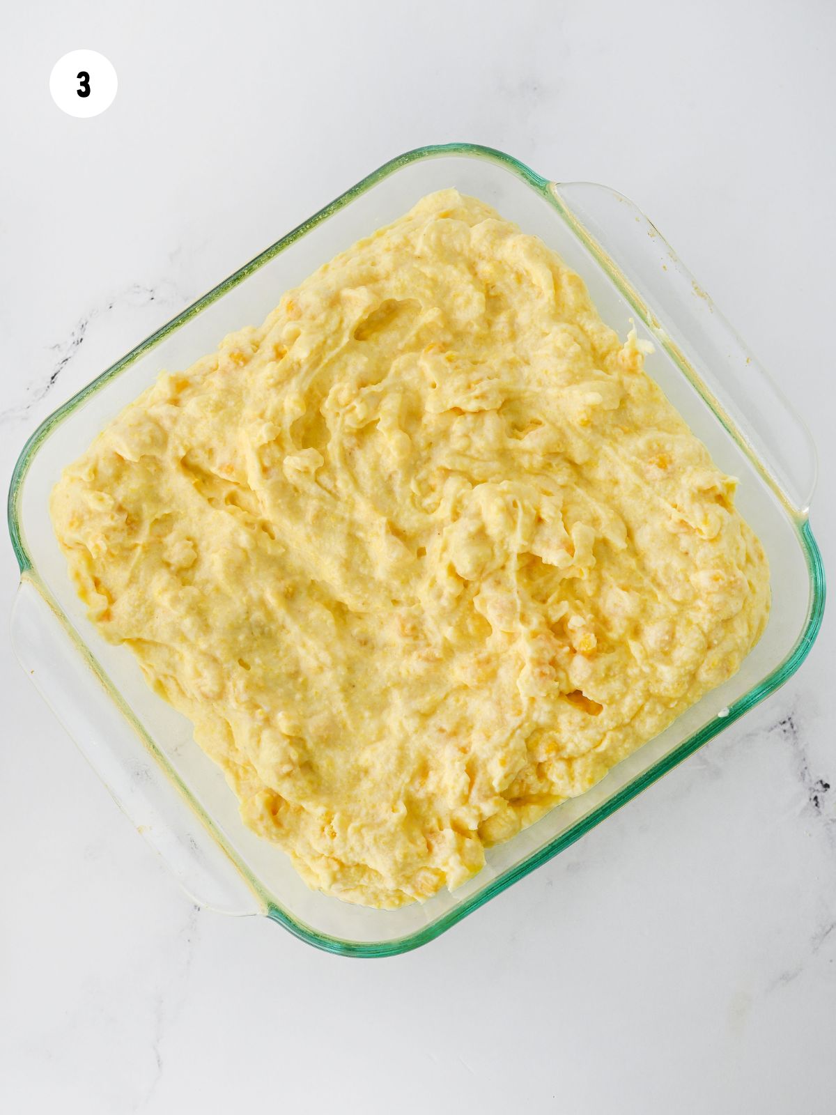 Corn pudding batter in a square baking dish.