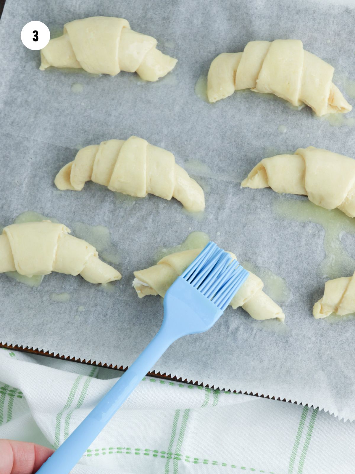 Blue silicone pastry brush adding butter to the rolls.