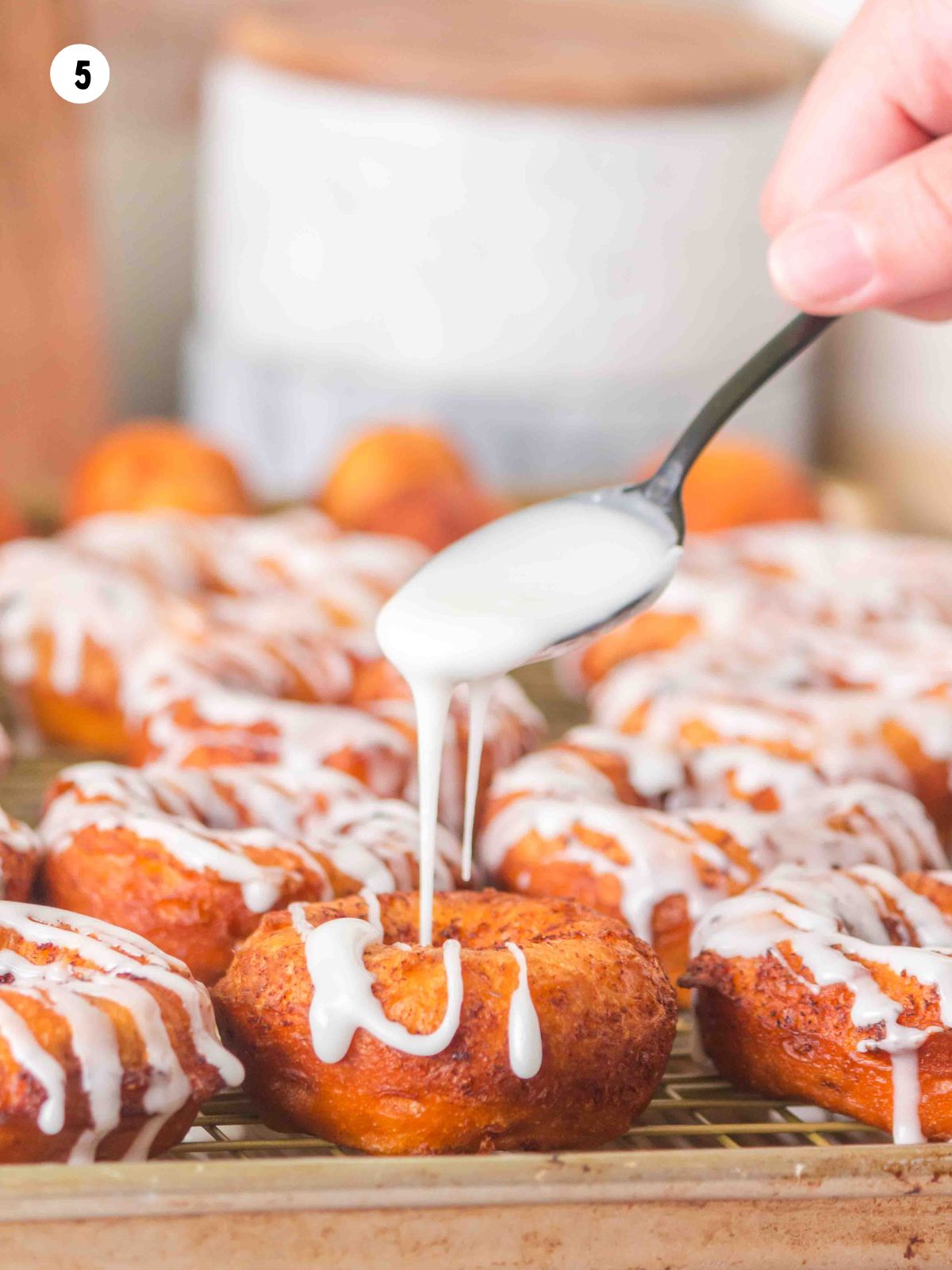 Spoonful of icing drizzling on the cinnamon roll donut.