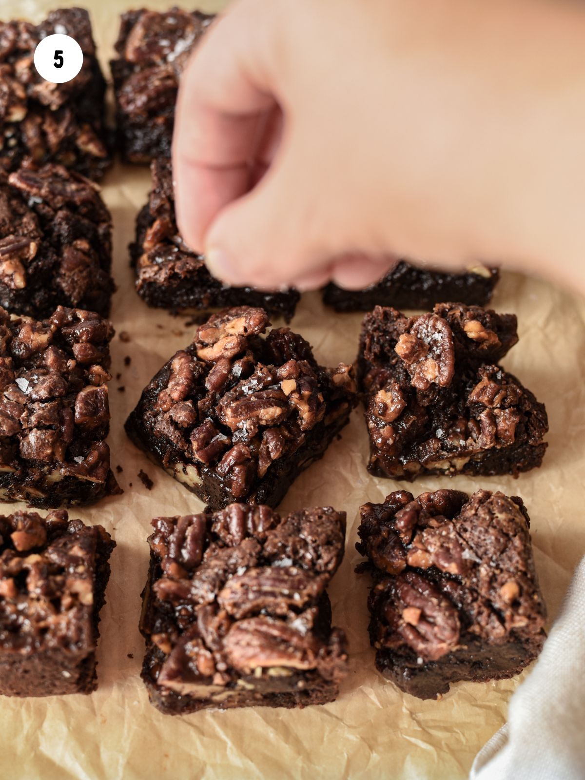 Hand adding flaky sea salt on top of the brownies.