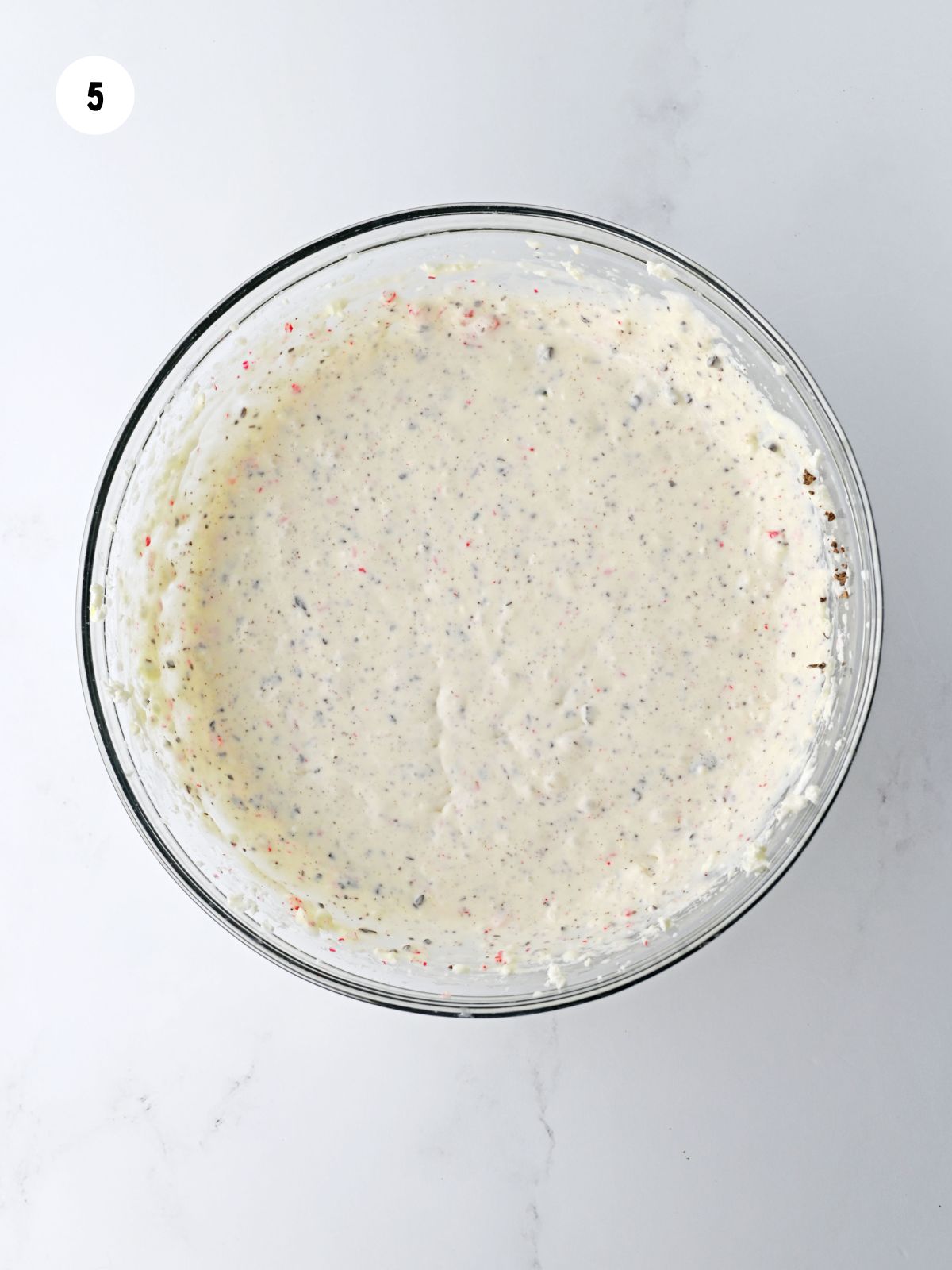 Mixing bowl of cheesecake filling with peppermint pieces and chopped chocolate chips folded in.