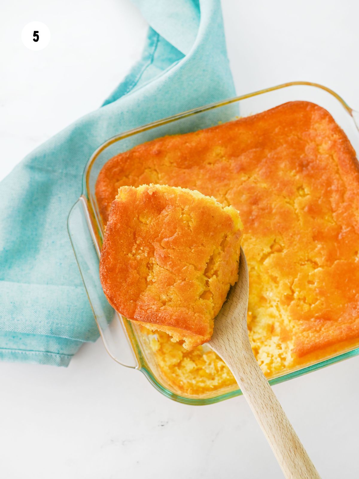 Spoonful of corn bread pudding casserole being taken out of the dish.