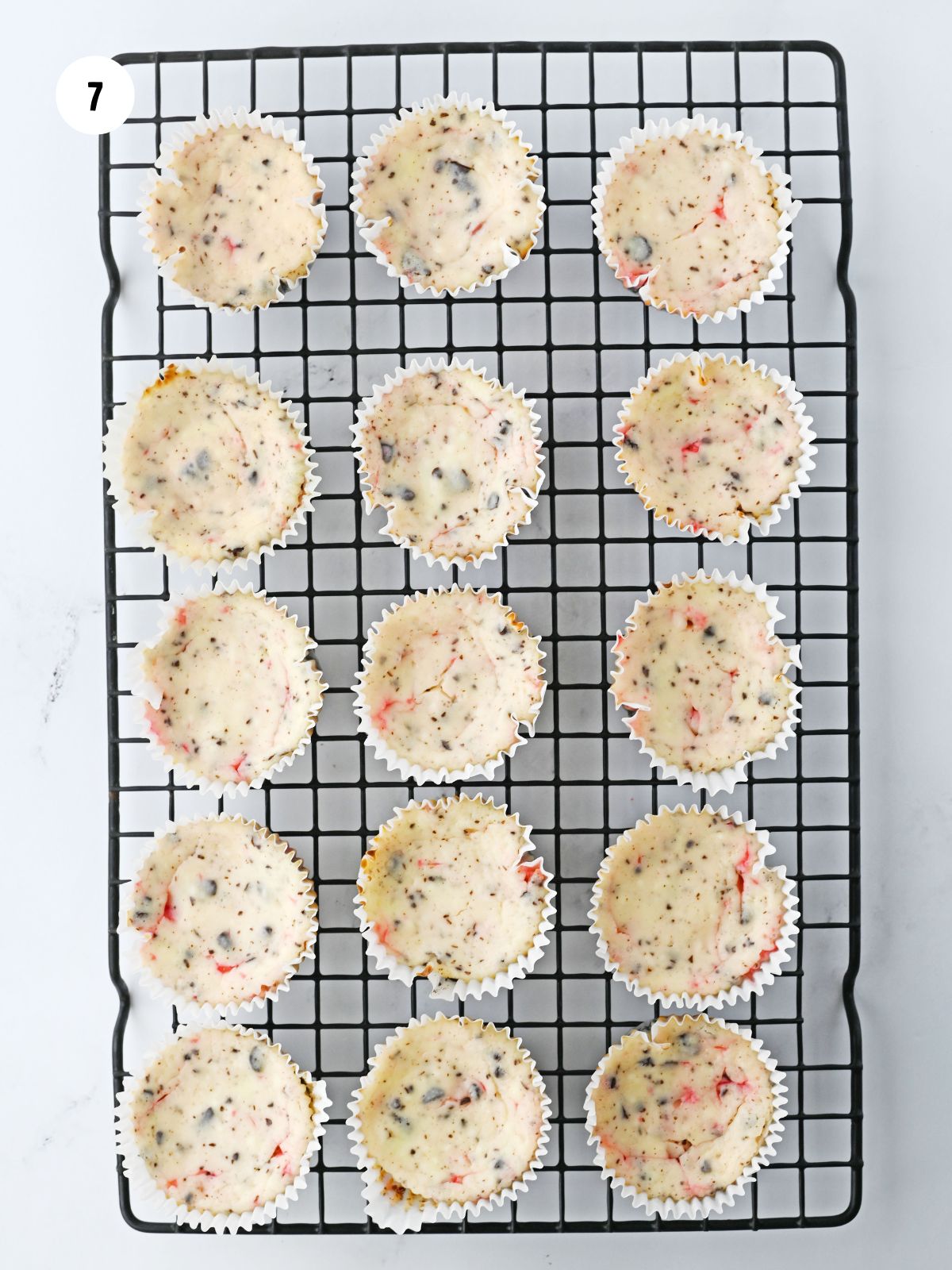 Cooling rack filled with baked mini cheesecakes.