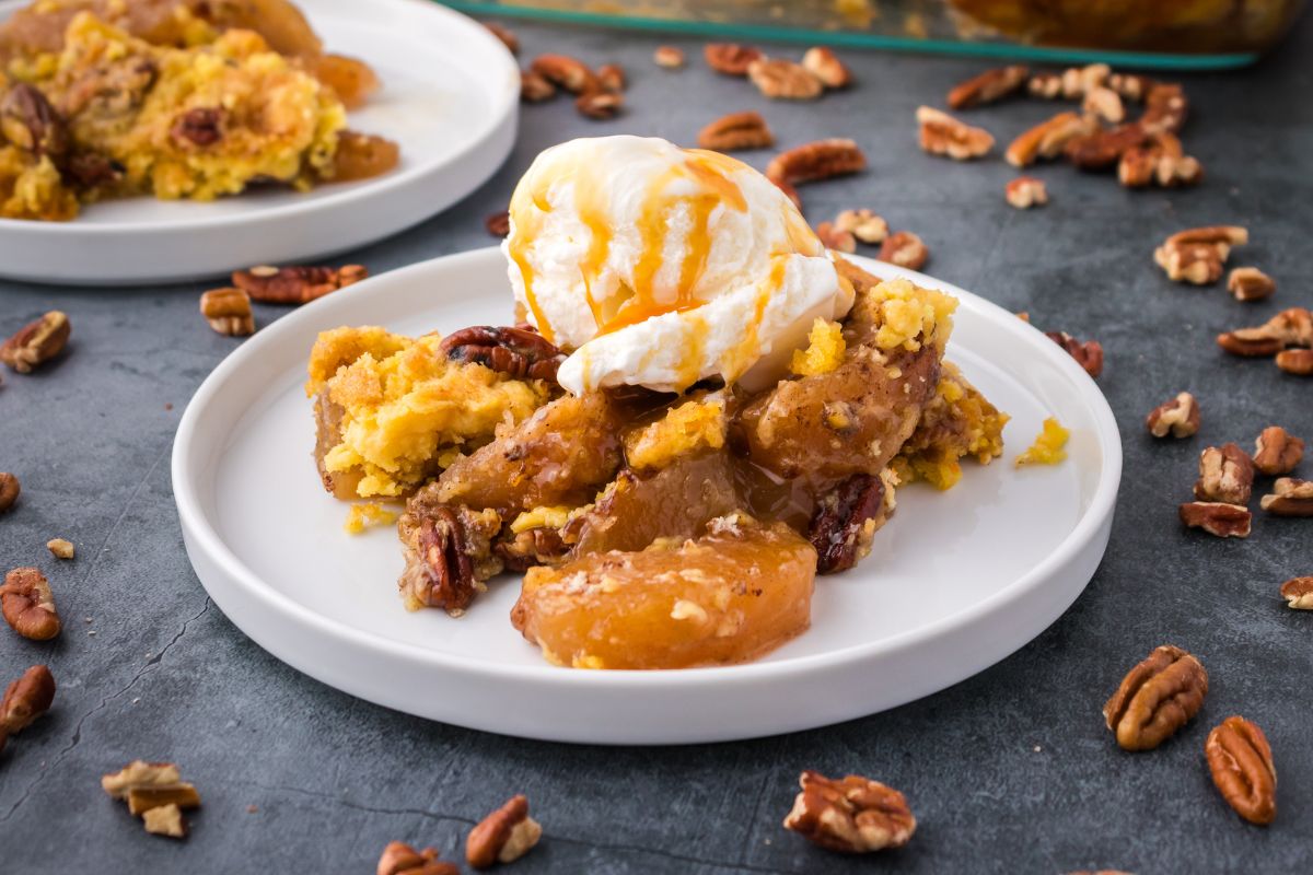 Apple Dump Cake served with a scoop of vanilla ice cream and a drizzle of caramel. Chopped pecans are scattered around the plate.