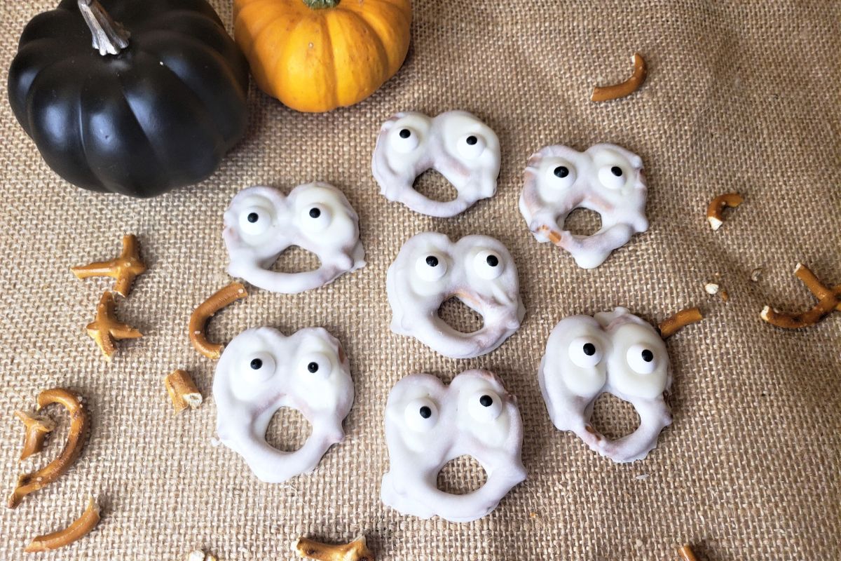 Chocolate Dipped Ghost Pretzels with little black and orange pumpkins in the background.