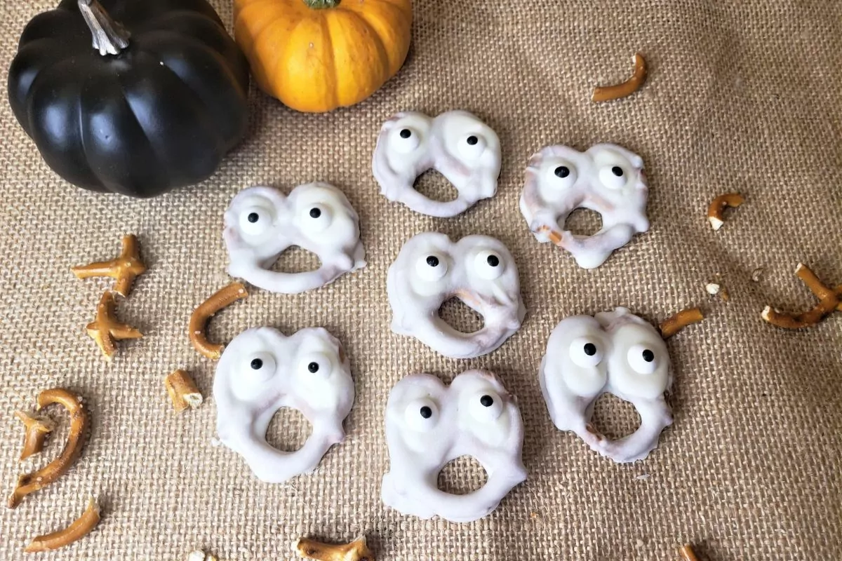 Chocolate Dipped Ghost Pretzels with little black and orange pumpkins in the background.