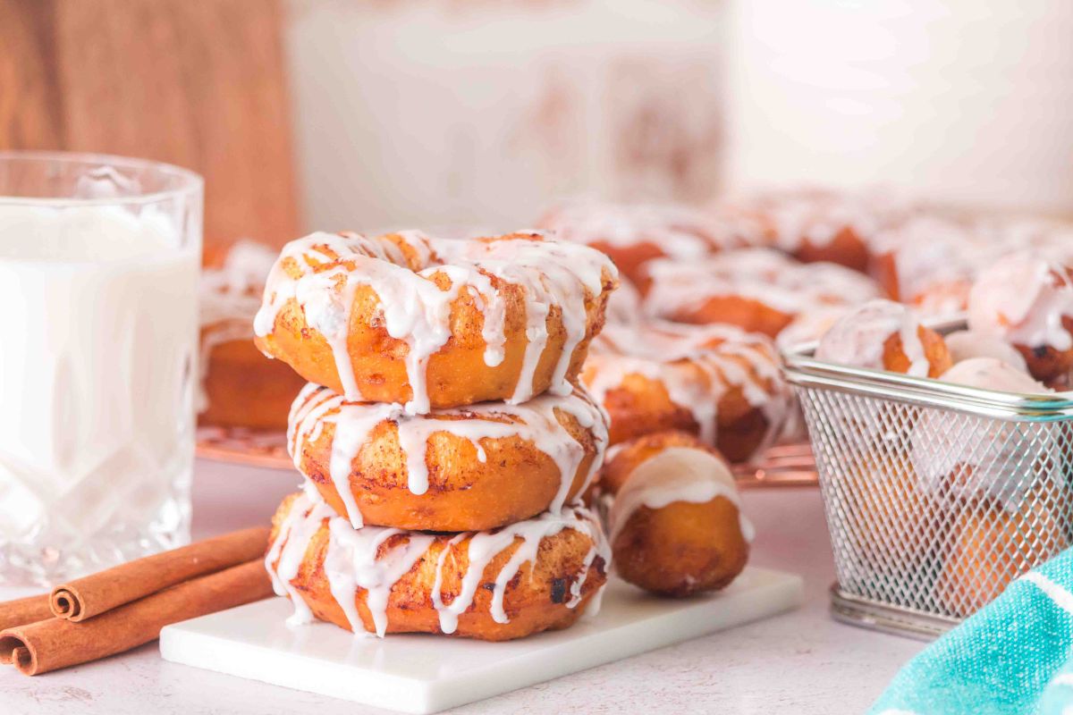 Stack of 3 cinnamon roll donuts. Glazed donut holes next to the stack. Glass of milk to the left.