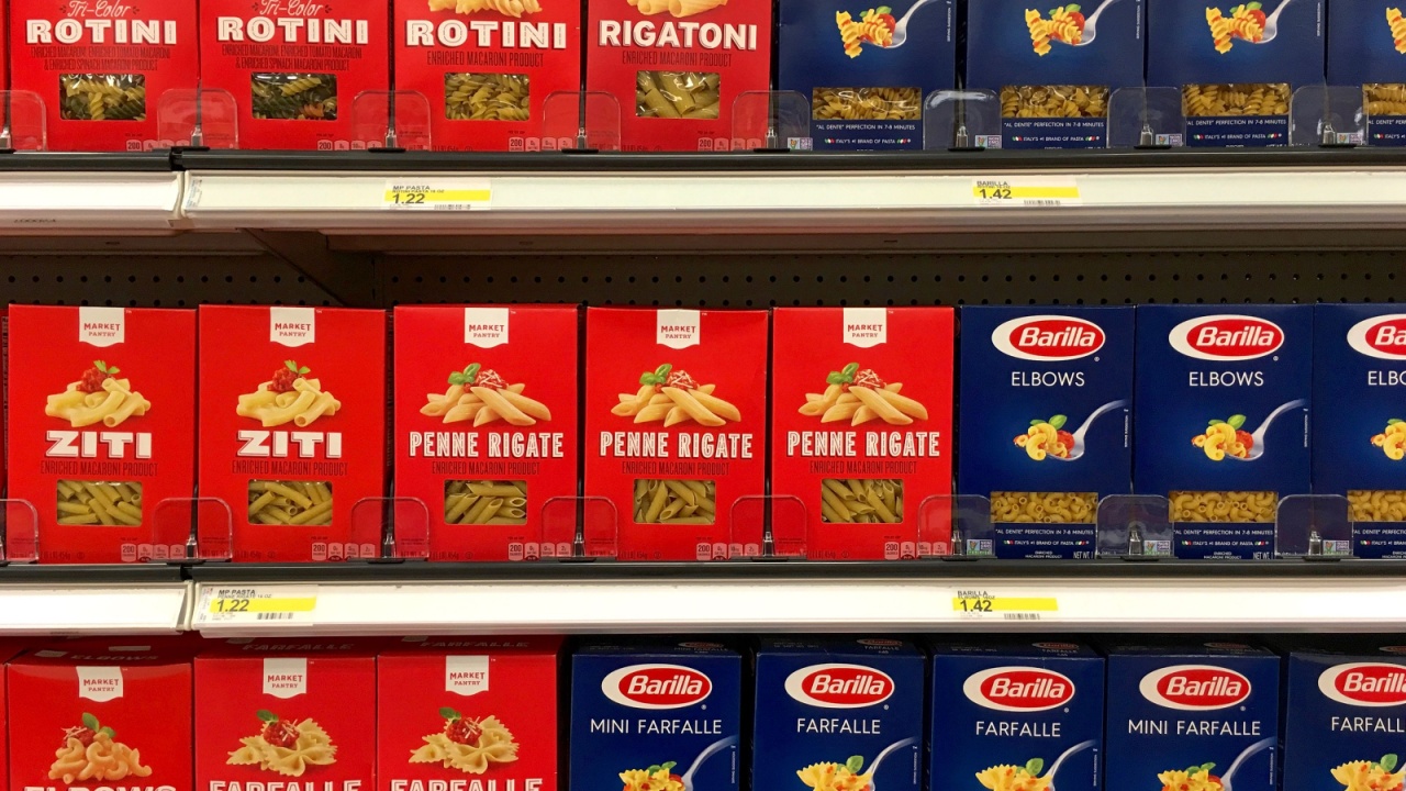 Grocery store shelf with boxes of generic brand Market Pantry pasta next to name brand Barilla pasta