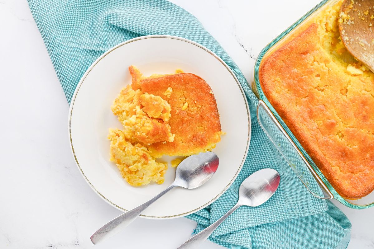 Scoop of Jiffy Corn Bread Pudding Casserole served on a white plate next to the baking dish.