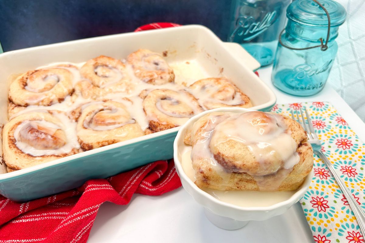 Teal 9x13 baking dish with cinnamon rolls and one taken out and served on a white dish.